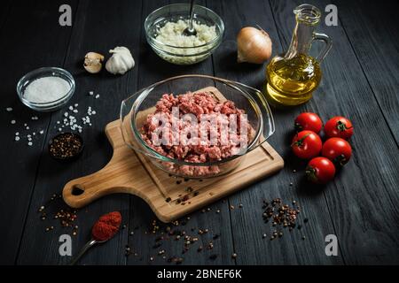 Hacher la viande hachée crue avec les ingrédients sur une table en bois noir. Maison. Banque D'Images