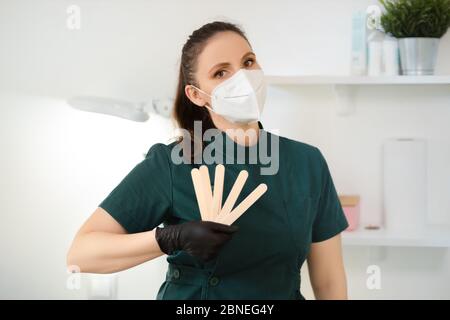 La femme maître de la cire ou de la sugarde tient une spatule en bois portant un masque médical en salon Banque D'Images