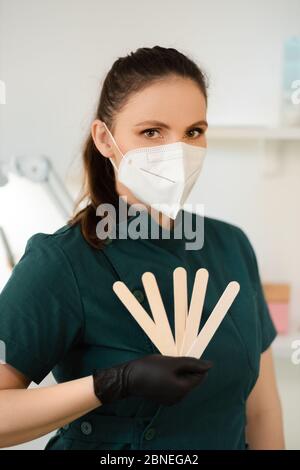 La femme maître de sugarde ou de cire tient une spatule en bois portant un masque médical Banque D'Images