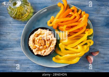 Vue de dessus d'un paprika jaune vif et orange avec trempette houmous sur fond bleu Banque D'Images