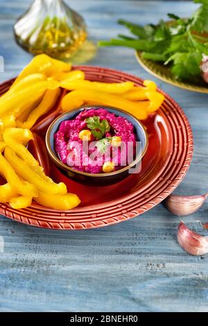 Photo verticale d'un plateau rouge vif avec bâtonnets de paprika jaune et houmous de betterave sur fond bleu Banque D'Images