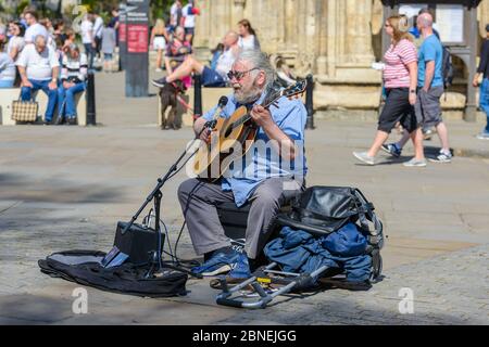 York, North Yorkshire / Angleterre : un busseur joue de la guitare sur une place animée par York Minster, dans un après-midi ensoleillé d'avril. Banque D'Images