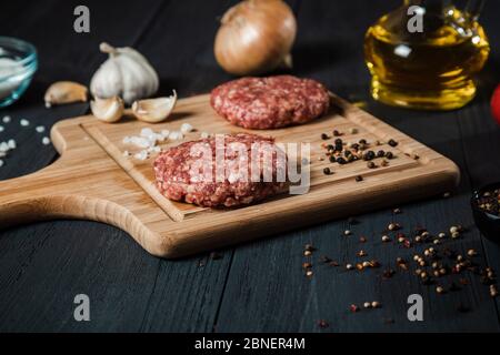 Des côtelettes de viande hachée avec les ingrédients sur la table en bois noir. Cuisine maison. Banque D'Images