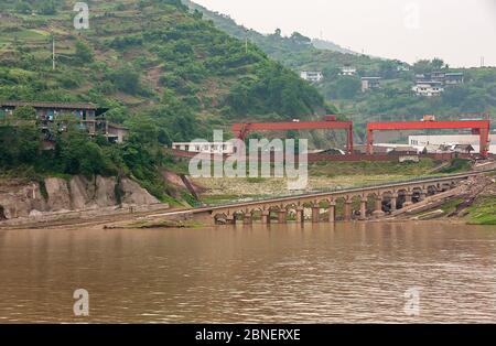 Myaoyinan, Chongqing, Chine - 8 mai 2010 : fleuve Yangtze. Cale et grands ponts de grue derrière l'eau brune, au chantier naval de Chiandong. Green Mountain sl Banque D'Images