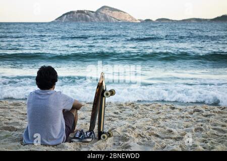 Photo incroyable d'un jeune homme assis sur une plage et en admirant la mer Banque D'Images