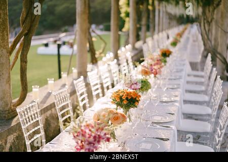 Réception de table de mariage. Une très longue table de mariage allant dans la perspective. Bouquets de roses jaunes, orange et roses sur les tables. Chaises en verre Banque D'Images