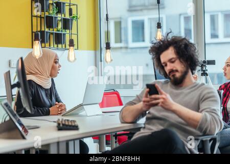 Un gars barbu avec afro coiffure parler sur son téléphone tout en étant entouré de ses collègues multiethniques. Homme d'affaires travaillant dans un départ décontracté Banque D'Images