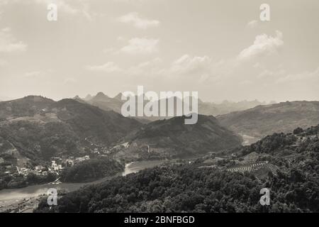 Photo en niveaux de gris d'une belle petite ville dans les collines par la rivière capturée du sommet d'une colline Banque D'Images