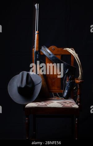Fusil à levier, revolver, corde, chapeau de cow-boy et chaise à fond noir, verticale Banque D'Images