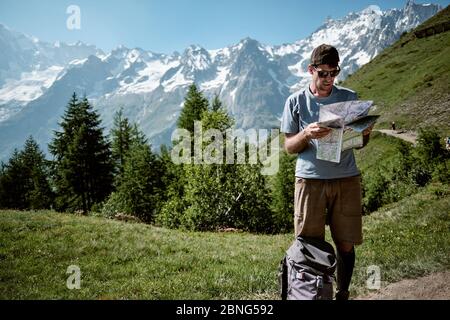 Jeune homme regardant la carte des sentiers tout en randonnée dans les montagnes dans une journée ensoleillée d'été Banque D'Images