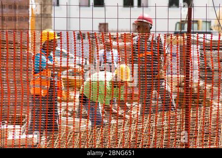 Les ouvriers de la construction équipés de casques de sécurité se tiennent derrière une clôture de protection Banque D'Images