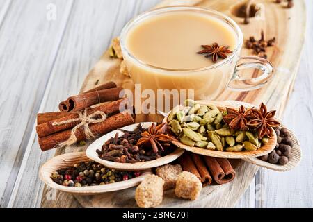 Boisson traditionnelle indienne - thé masala aux épices. Cannelle, cardamome, anis, sucre, clous de girofle, poivre sur fond de bois clair Banque D'Images