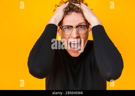 Image d'un jeune homme en colère dans des lunettes criant et groulant sa tête isolée sur fond jaune Banque D'Images