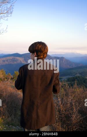 Arrière de l'adolescent solitaire mâle debout et en admirant une vue sur une belle vallée dans les montagnes de Cévennes, en France, en fin d'après-midi en hiver Banque D'Images