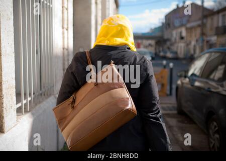 Vue arrière d'une femme adulte portant un hijab jaune et portant un sac à main, en descendant une rue à Montpellier, France Banque D'Images