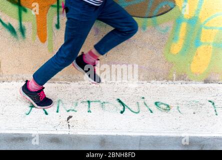 Détail des jambes et des pieds avec les entraîneurs d'une jeune fille de sept ans qui court devant un mur recouvert de graffiti urbains à Figuerolles, Montpellier, FRA Banque D'Images