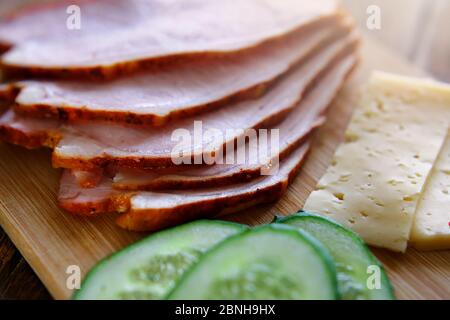 Trancher du jambon, des concombres et du fromage avec des pains fins et grossiers se trouvent sur une planche en bois. Banque D'Images