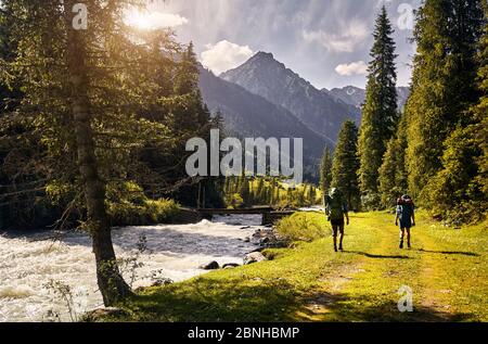 Deux hommes avec de grands sacs à dos se promonent dans la forêt de la vallée de la montagne dans le parc national de Karakol, Kirghizistan Banque D'Images