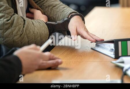 Stuttgart, Allemagne. 15 mai 2020. L'accusé, dans un procès pour fraude, porte des menottes et place un dossier à sa place dans une salle d'audience du tribunal régional. L'ancien chef de la coopérative d'habitation de Geno, en tant que responsable de la coopérative déjà insolvable, aurait trompé de nouveaux membres et les aurait fait payer un total de plus de deux millions d'euros. Credit: Marijan Murat/dpa/Alay Live News Banque D'Images