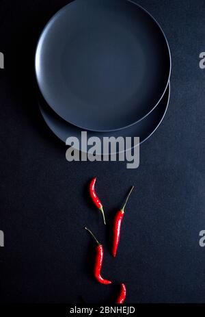 Composition minimaliste de piments rouges et deux assiettes en céramique sur fond noir Banque D'Images