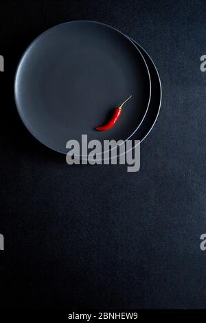 Composition minimaliste de piment rouge dans la plaque en céramique à la table noire Banque D'Images