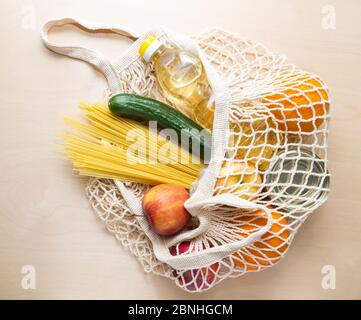 Livraison de nourriture. Le filet de sac avec la nourriture: Huile, spaghetti, pomme, orang, concombre, marchandises pour les dons pendant la quarantaine. Banque D'Images