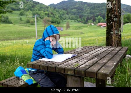 Jeune garçon homeschooling sur une table en bois dehors dans la nature pendant le voyage familial pendant la crise du virus Corona, Europe, Slovénie Banque D'Images