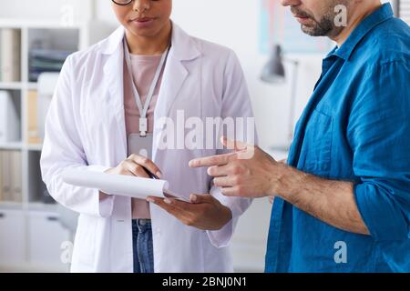 Gros plan d'une femme médecin montrant une carte médicale dans ses mains et montrant quelque chose à la patiente Banque D'Images