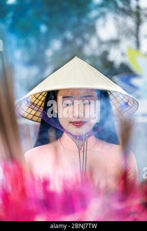 Une jeune femme vietnamienne dans un chapeau conique faisant des offrandes d'encens à un temple bouddhiste, Hue, Vietnam, Indochine, Asie du Sud-est, Asie Banque D'Images