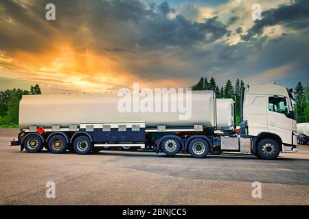 Semi-camion-citerne blanc stationné sur une cour d'asphalte, vue latérale, avec un magnifique ciel de coucher de soleil sur l'arrière-plan. Éléments reconnaissables supprimés. Banque D'Images