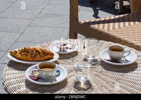 Café dans une tasse blanche avec cuillère, croissant et verres d'eau sur la table, café ou bar extérieur, concept petit déjeuner Banque D'Images