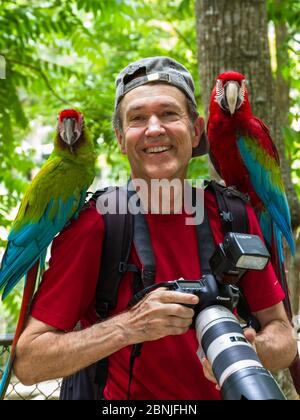 Le photographe allemand de la faune Konrad Woit avec la macaw militaire (Ara militararis) et la macaw rouge et verte (Ara chloroptera) et son appareil photo, Trinidad Banque D'Images