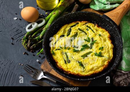 Omelette aux asperges saines. Omelette aux oeufs avec asperges et oignons dans une poêle en fonte sur un comptoir en pierre. Copier l'espace. Banque D'Images