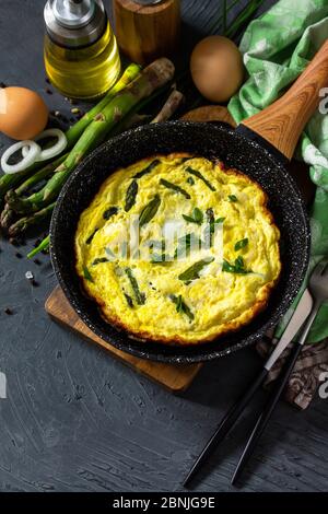 Omelette aux asperges saines. Omelette aux oeufs avec asperges et oignons dans une poêle en fonte sur un comptoir en pierre. Copier l'espace. Banque D'Images