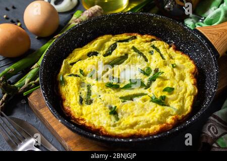 Omelette aux asperges saines. Omelette aux oeufs avec asperges et oignons dans une poêle en fonte sur un comptoir en pierre. Banque D'Images