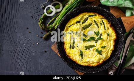 Omelette aux asperges saines. Omelette aux oeufs avec asperges et oignons dans une poêle en fonte sur un comptoir en pierre. Vue de dessus de l'arrière-plan de la mise à plat Bannière. Banque D'Images