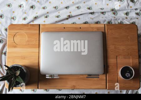 Vue en grand angle sur un ordinateur portable avec deux plantes sur le dessus d'un bureau escamotable portable reposant sur un lit à la lumière du jour. Banque D'Images