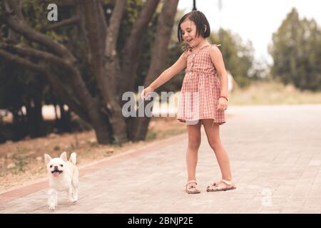 Drôle enfant fille 3-4 ans jouer avec chien dans le parc portant robe élégante à l'extérieur. Ensemble. Amitié. Banque D'Images