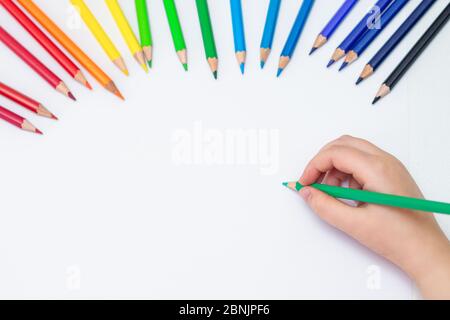 Vue de dessus du dessin de la main de bébé avec un crayon vert sur papier blanc avec le jeu de crayons de couleur. Concept de peinture pour enfants. Copier l'espace pour le texte. Maquette. Banque D'Images