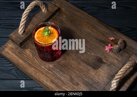 Cocktail traditionnel rouge vif avec whisky sur une planche en bois. Décoration avec des cônes et des petites fleurs roses. Exemple de service parfait Banque D'Images