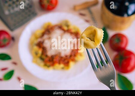 Un cappelletti sur une fourchette et en arrière-plan une table avec la cuisine italienne typique Banque D'Images
