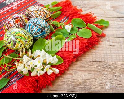 joliment décoré à la main des œufs de pâques orthodoxes roumains avec des motifs traditionnels sur un tissu rouge avec des fleurs d'acacia de côté Banque D'Images