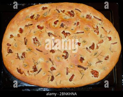 PAIN DE FOCACCIA CUIT DANS UN PLATEAU DE CUISSON AVEC DES TOMATES SÉCHÉES AU SOLEIL, NAPPÉES DE ROMARIN, D'AIL, D'HUILE D'OLIVE Banque D'Images