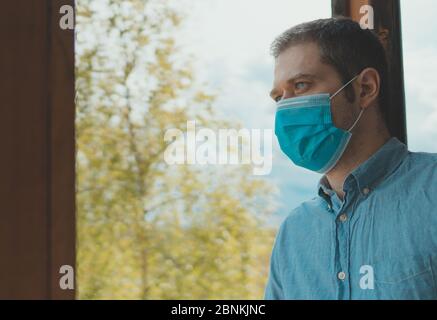 Homme dans le masque médical se tient sur le balcon et respire l'air frais. Restez à la maison. Banque D'Images