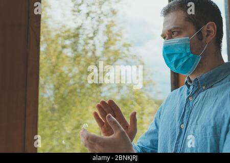 L'homme en masque médical se tient sur le balcon et applaudit aux médicaments. Restez à la maison. Banque D'Images