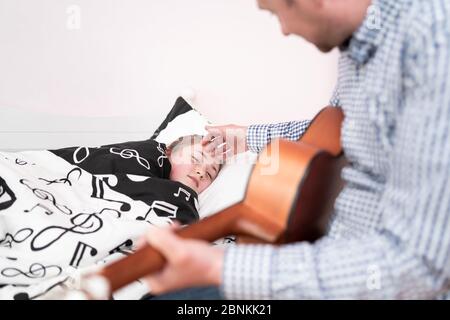 Le père s'occupe de sa fille malade. Amour parfait. Garde d'enfants. Un homme avec une guitare vérifie le bien-être d'un enfant. Papa joue pour sa petite fille Banque D'Images