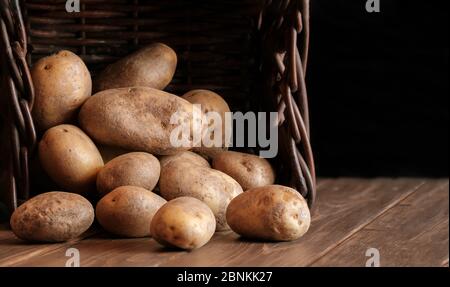 beaucoup de pommes de terre dans un panier en osier légumes crus encore vie chiaroscuro légumes sur parquet rustique noir fond foncé avec espace de copie Banque D'Images