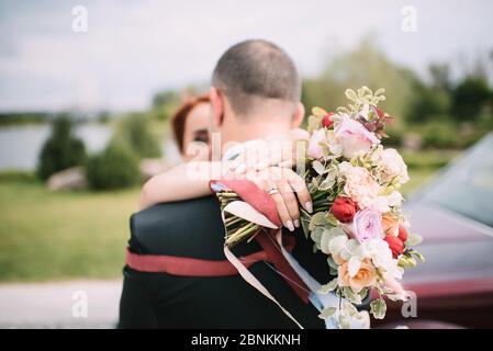 Gros plan du bouquet de roses d'une mariée, eucalyptus blanc, bleu, rouge, noué avec des rubans blancs. La mariée tient un bouquet dans sa main Banque D'Images