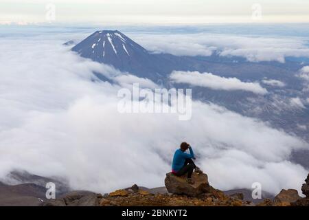 Une femme grimpeur se trouve sur un rocher sur le mont Ruapehu et regarde vers le mont Ngauruhoe, dans le parc national de Tongariro, en Nouvelle-Zélande Banque D'Images