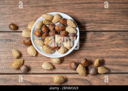 dans un bol blanc sur une table brune, mélanger les noix d'amandes et les noisettes avec la coque Banque D'Images